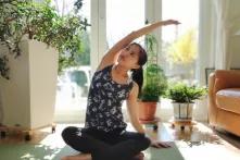 Lina Lam sitzt in einem lichtdurchfluteten Zimmer auf einer Yoga-Matte im Schneidersitz und macht eine Dehnübung mit ihrem rechten Arm