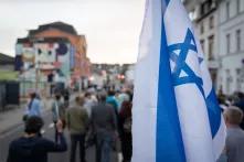 Bei einem Schweigemarsch in Solidarität mit Israel in Saarbrücken sind auf einer Straße laufende Menschen von hinten zu sehen, im Vordergrund eine Israel-Flagge. 
